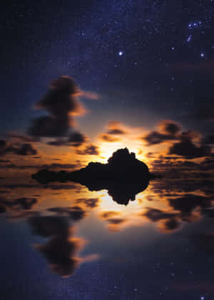 在繁星點點、雲朵發光的夜空下，岩石島嶼的輪廓倒映在水中。 — 星星 壁紙