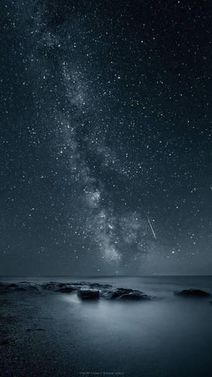 在繁星點點的夜空下，銀河系位於黑暗的海洋岩石之上 — 星空動畫 壁紙