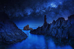 繁星點點的夜空，銀河在平靜的藍色海洋和岩石懸崖上空。 — 星空動畫 壁紙