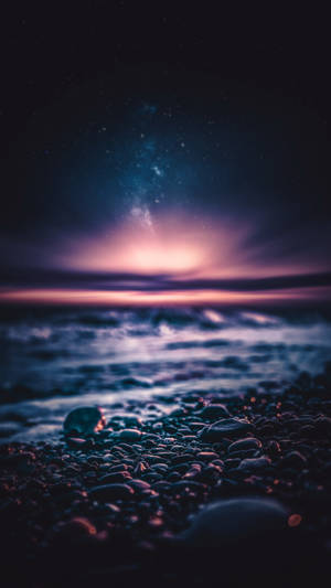 繁星點點的夜空下，鵝卵石海灘與溫柔的海浪。 — 舊金山 iPhone 壁紙