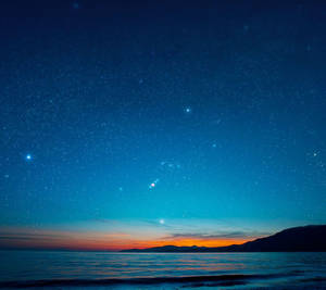海洋上的星空，地平線上的山脈發出橙色光芒 — Xiaomi 壁紙