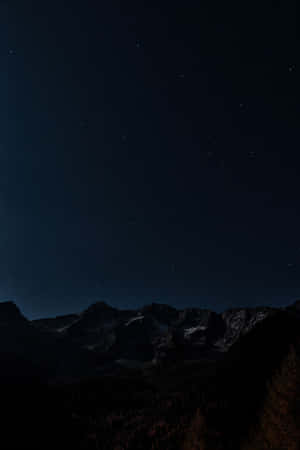 繁星點點的夜空下，黑暗的山脈，山頂有雪，下方有森林。 — 黑夜 壁紙