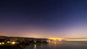 夜晚的沿海小鎮，星空璀璨，燈光倒映在水面上 — 夕陽天空 壁紙