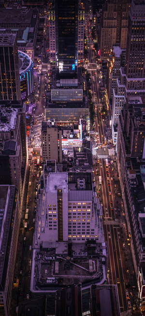 密集城市景觀的夜晚鳥瞰圖，街道和建築物閃爍。 — iPhone 16 Pro 壁紙
