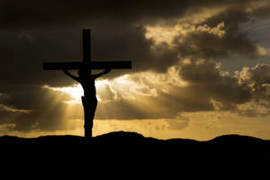 日落時分，耶穌在十字架上的剪影，金色光芒穿透烏雲。