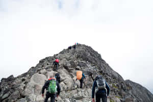 一群登山者在多雲的天空下，背著背包攀爬陡峭的岩石山。 — 山坡 壁紙