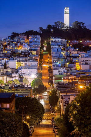 暮色中舊金山陡峭街道的景色，遠處可見科伊特塔。 — 舊金山 iPhone 壁紙