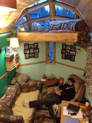 男子在舒適的木屋中閱讀，有木樑和書架。 — 首頁 壁紙