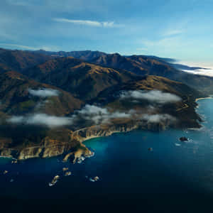 沿海高速公路沿懸崖蜿蜒，海洋與山脈在藍天下。 — iPad Air 11 壁紙