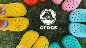 鮮豔色彩的Crocs涼鞋圍繞帶有Crocs標誌的草地區域排列。 — Crip 壁紙