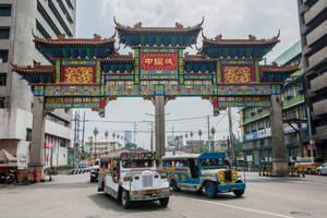 色彩繽紛的吉普尼車在繁忙都市街道上行駛於傳統中式牌坊下。 — 馬尼拉 壁紙