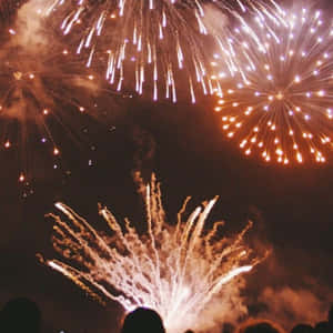 煙火在人群上方以金色和紫色的爆發照亮夜空。 — 慶祝 壁紙