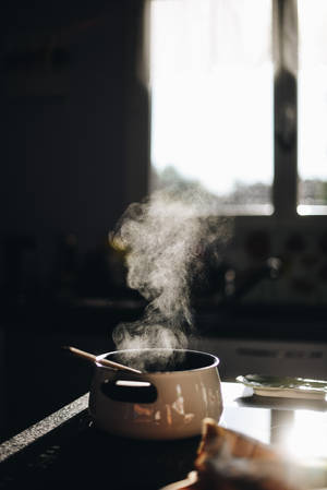 蒸氣從白色鍋中升起，鍋放在廚房檯面上，有明亮窗光。 — 烹飪 壁紙