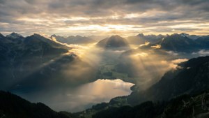 黎明時分，陽光穿過雲層，照耀在山間湖泊上。 — 3440x1440 壁紙