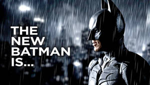 蝙蝠俠在雨中，身後有城市燈光和文字「THE NEW BATMAN IS...」。 — 蝙蝠俠 2022 壁紙