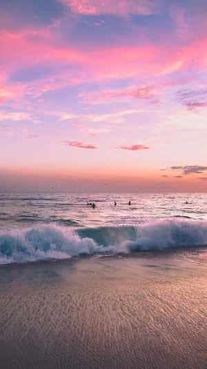 衝浪者在粉紅色日落海灘的海浪上 — 海灘 iPhone 壁紙