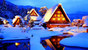 積雪的傳統日本房屋在夜間發光，冰池中倒映著山景。 — 冬季風景 壁紙