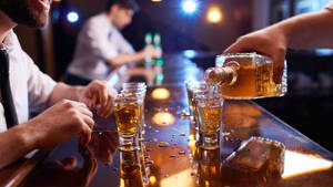 手在昏暗的吧檯上將琥珀色烈酒倒入小酒杯。 — 酒吧 壁紙