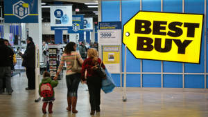 購物者（包括一名兒童）走過帶有促銷標誌的 Best Buy 零售店。 — 最佳購買 壁紙
