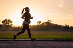 一個人在日落時分在小路上慢跑，背景有草地和樹木。 — Running 壁紙