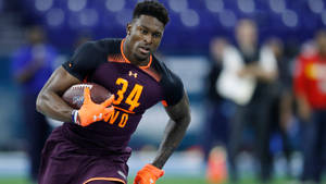 身穿栗色和橙色裝備的橄欖球運動員在訓練中帶著球奔跑。 — Dk Metcalf 壁紙