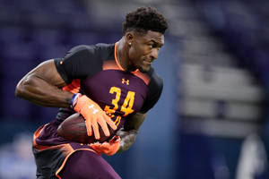 身穿栗色和橙色球衣的美式足球員在室內帶球奔跑。 — Dk Metcalf 壁紙