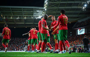 身穿紅綠球衣的足球員在夜間燈光明亮的球場上慶祝進球。 — FIFA 世界盃 壁紙