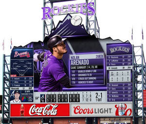 棒球選手 Nolan Arenado 在一個顯示比賽統計數據和球隊標誌的記分牌前。 — 運動 壁紙