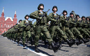 身穿迷彩軍服的士兵在紅色建築附近的鵝卵石街道上列隊行進。 — 莫斯科 壁紙