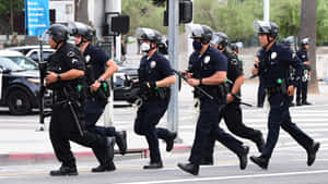 身穿防暴裝備的警察在白天跑過城市街道。 — 警察 GIF 壁紙