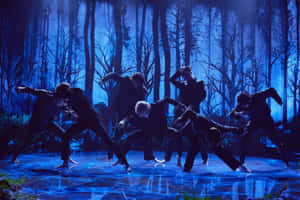 身穿黑色西裝的舞者在藍色燈光舞台上，以森林為背景表演。 — MacBook Pro 14 壁紙