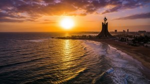 金色海浪與沙灘和城市旁邊的顯眼紀念碑的海岸日落。 — ROG Ally 壁紙