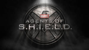 S.H.I.E.L.D.標誌在黑暗煙霧環境中被聚光燈照亮，帶有Marvel品牌。 — 漫威標誌 壁紙