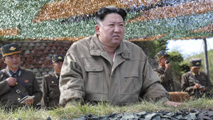 金正恩在戶外與身穿軍服的軍人坐在一起。 — 南韓 壁紙