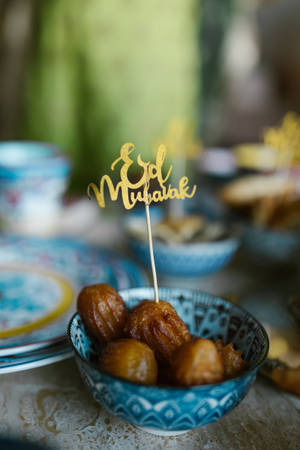 藍色圖案碗盛載炸麵糰球，配上金色 Eid Mubarak 標誌。 — 慶祝 壁紙
