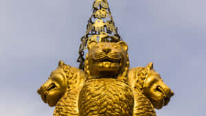 金色三頭獅子雕像，戴著王冠，襯以藍天。 — 廟宇 壁紙
