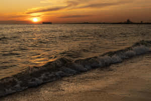 海洋上的夕陽，波浪沖刷海岸，遠處有船和燈塔。 — 日落 壁紙