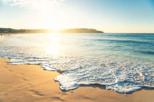 海洋上的日出，海浪沖刷沙灘和遠處的衝浪者 — MacBook Air 13 壁紙