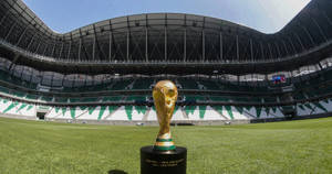 藍天下空蕩體育館草地上的金色世界盃獎盃 — 卡達 壁紙