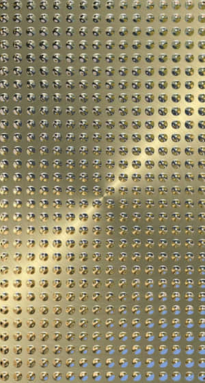 金色穿孔金屬牆，帶有重複的圓形孔洞和光線反射。 — Surface 壁紙