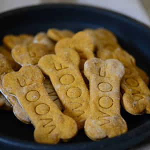 一堆金色骨頭形狀的狗零食，上面壓印著'WOOF'，放在一個深色碗裡。 — 狗狗藝術 壁紙