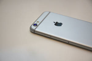 銀色 iPhone 6s 平放在純色表面上，顯示背面標誌和相機。 — 太空 iPhone 壁紙