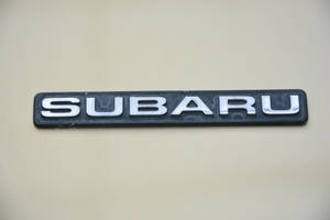 米色引擎蓋上的銀色 Subaru 標誌，有輕微磨損。 — 昴 壁紙