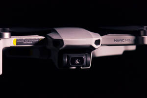 銀色DJI Mavic Mini無人機，帶相機和手臂指示，黑色背景。 — 網路攝影機 壁紙