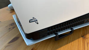 銀色PlayStation 5主機置於淺藍色底座上，放在木桌上 — PS5 動態圖片 壁紙