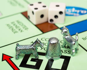 銀色狗、貓和頂針遊戲棋子放在大富翁棋盤上，附有骰子。 — 地產大亨 壁紙