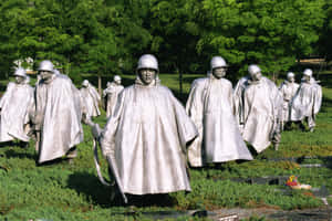 銀色的士兵雕像穿著斗篷，在有綠樹的草地公園上行進。 — MacBook Air 壁紙