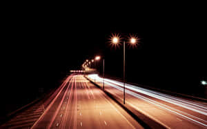 夜晚高速公路，街燈下紅色和白色汽車燈光形成條紋。 — 城市燈光 壁紙