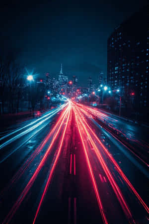夜間濕漉漉的城市高速公路上，汽車的紅色和藍色光軌，遠處有發光的天際線。 — 城市風景 壁紙