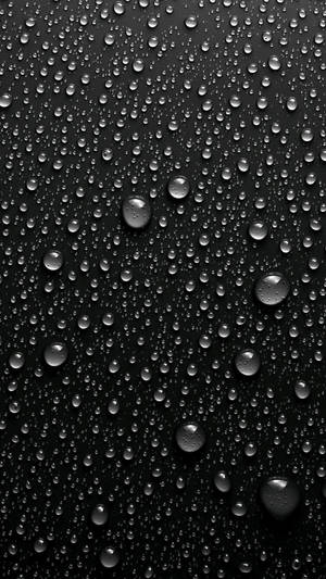 黑色表面上反射光線的雨滴特寫。 — 悟空黑 iPhone 壁紙